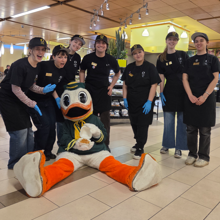 student employees in dining uniforms smiling as they pose with the Duck mascot