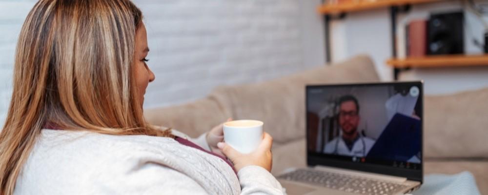 woman on video call with care provider, drinking coffee on her couch