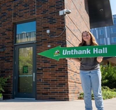 Student holding a residence hall sign that points to a door